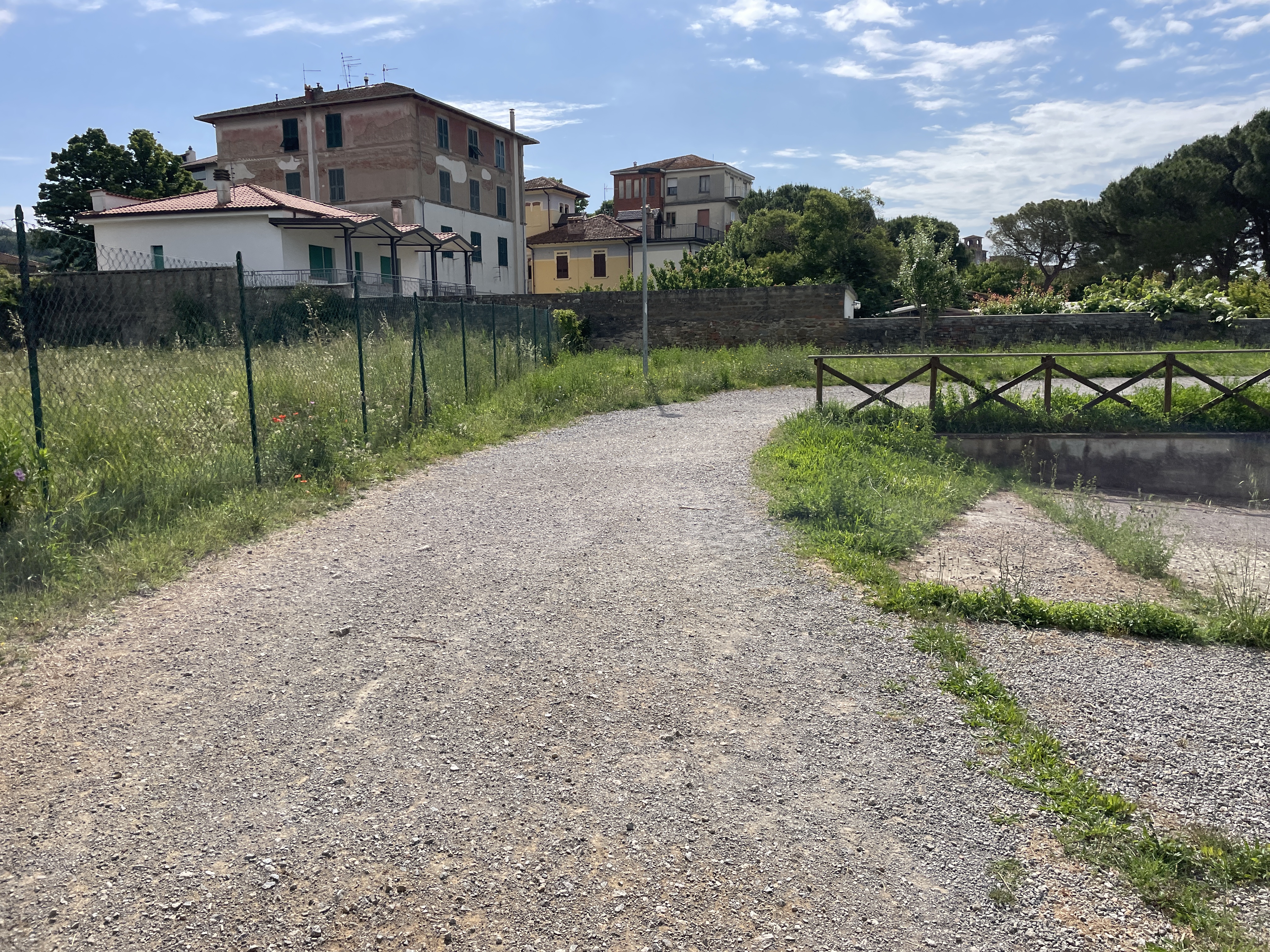 Dirt bicycle path near houses in Passignano. Wire fence on left, wooden fence on right.